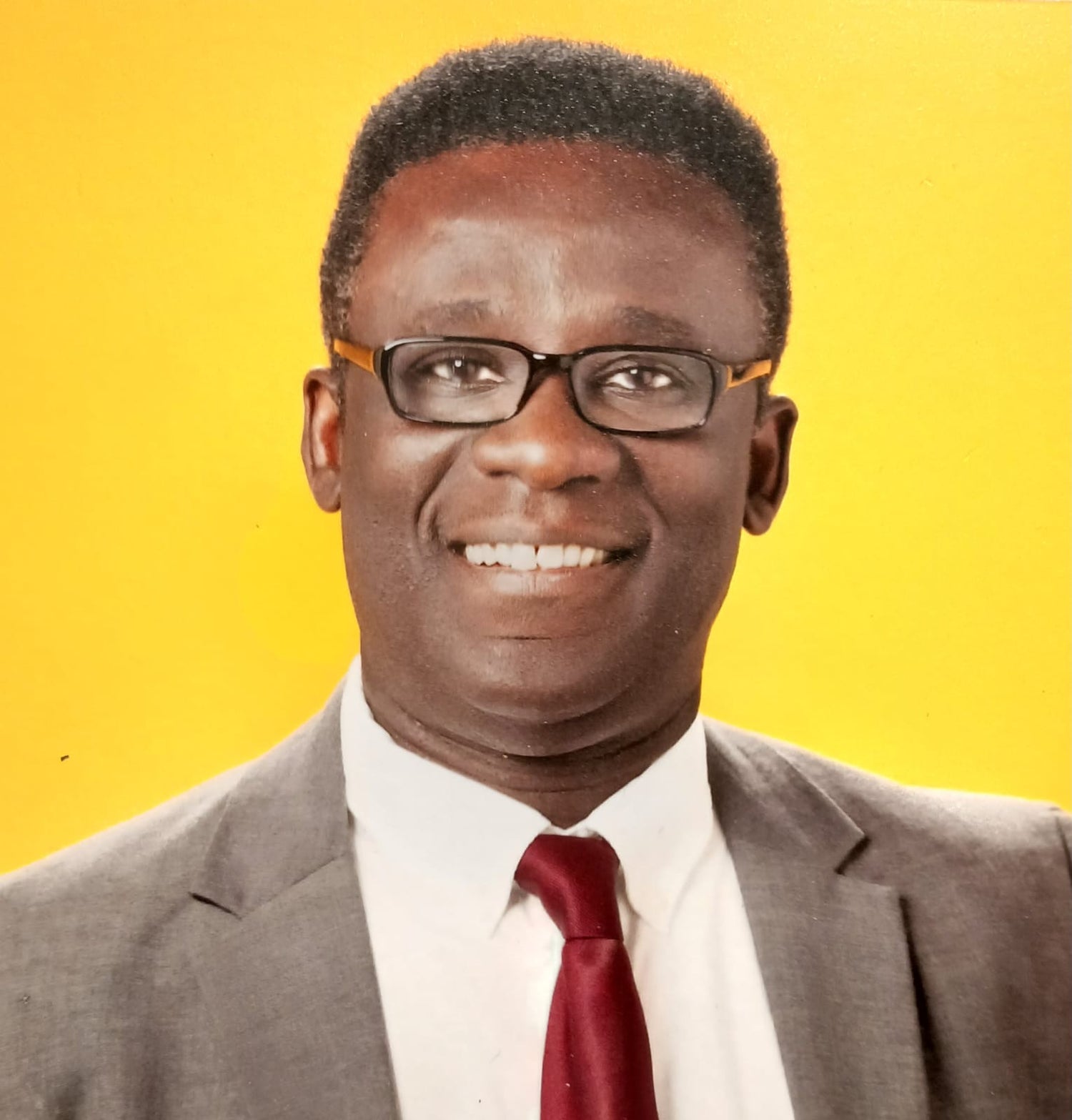 Mr. Marfo, a man wearing a grey suit with a red tie on a yellow background